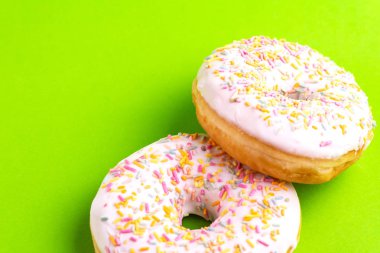 İki lezzetli vanilyalı donut ile parlak yeşil zemin üzerine serpin. Sağlıksız, ama lezzetli tatlılar. Uzay kopyalayın. Üstten görünüm