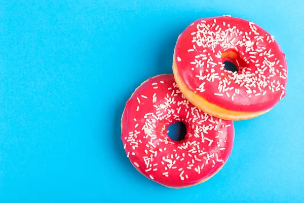 两个美味的粉红色甜甜圈 洒在明亮的蓝色背景 不健康 但好吃的糖果 复制空间 顶视图 — 图库照片