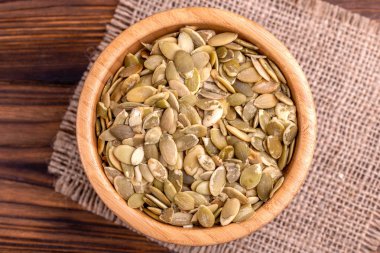 Çuval bezi peçete ahşap arka plan üzerinde ahşap kase taze kabak çekirdeği. Uzay kopyalayın. Üstten görünüm