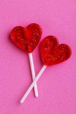 İki kırmızı tatlı lezzetli lolipop parlak pembe bir arka plan üzerinde kalp şeklinde. St. Valentine's day. Kopya alanı