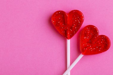 İki kırmızı tatlı lezzetli lolipop parlak pembe bir arka plan üzerinde kalp şeklinde. St. Valentine's day. Kopya alanı
