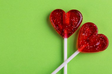 İki kırmızı tatlı lezzetli lolipop parlak yeşil arka plan üzerinde kalp şeklinde. St. Valentine's day. Kopya alanı