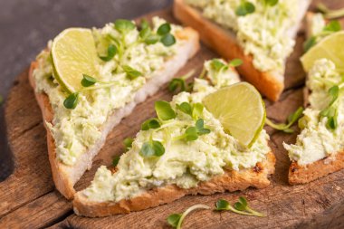 Tost avokado pate, taze microgreen ve kireç vintage kesme tahtası üzerinde. Karanlık beton arka plan. Sağlıklı ve lezzetli kahvaltı