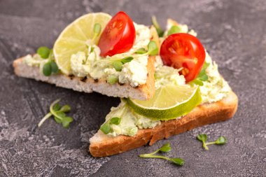 Tost avokado pate, taze microgreen ve karanlık beton zemin üzerine kiraz domates. Sağlıklı ve lezzetli kahvaltı