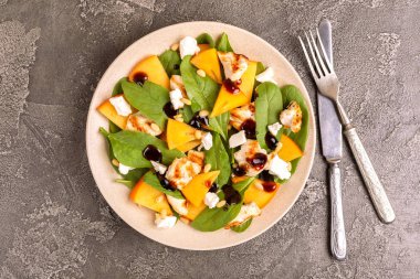 Ispanak, Trabzon hurması, ızgara tavuk fileto, beyaz peynir ve çam fıstığı ile egzotik salata tabağına bıçak ve çatal ile görev yaptı. Karanlık beton arka plan. Uzay kopyalayın. Üstten görünüm
