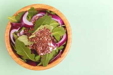 Açık yeşil arka planı üzerinde ahşap kase taze ıspanak, kırmızı soğan ve keten tohumu ile sağlıklı salata. Uzay kopyalayın. Üstten görünüm
