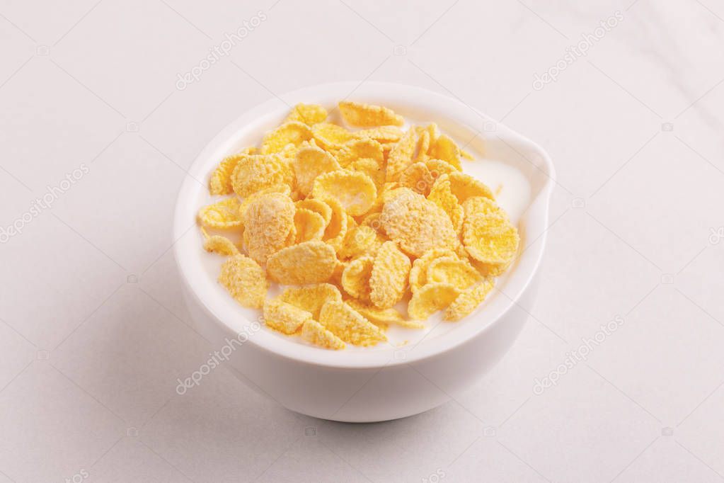 Fresh corn flakes in bowl with milk on light marble background. Healthy cereals breakfast. Copy space