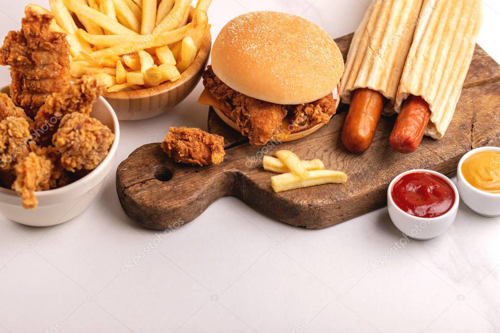 Delicious but unhealthy food with ketchup and mustard on vintage cutting board. Fast carbohydrates, junk and fast food. Light marble background.