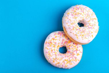 İki lezzetli vanilyalı donut ile parlak mavi zemin üzerine serpin. Sağlıksız, ama lezzetli tatlılar. Uzay kopyalayın. Üstten görünüm