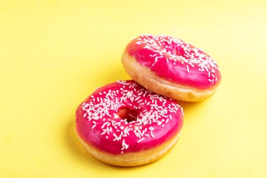 İki lezzetli pembe donut ile parlak sarı zemin üzerine serpin. Sağlıksız, ama lezzetli tatlılar. Uzay kopyalayın. Üstten görünüm