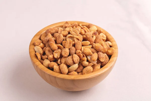 Roasted peanuts in wooden bowl on light marble background. Movie snacks. Copy space