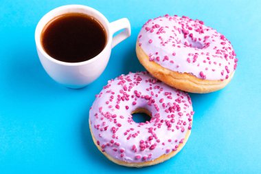 Serpin ve parlak mavi zemin üzerine koyu kahve fincan ile iki lezzetli leylak donut. Sağlıksız, ama lezzetli tatlılar. Uzay kopyalayın. Üstten görünüm