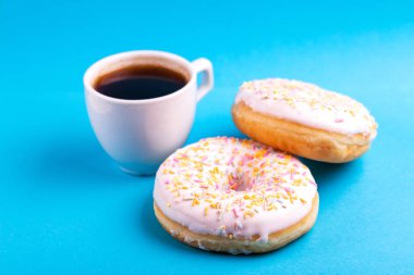 Serpin ve parlak mavi zemin üzerine kahve ile iki lezzetli vanilyalı donut. Sağlıksız, ama lezzetli tatlılar. Uzay kopyalayın. Yatay görünüm