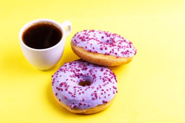 Serpin ve parlak sarı zemin üzerine kahve ile iki lezzetli leylak donut. Sağlıksız, ama lezzetli tatlılar. Uzay kopyalayın. Yatay görünüm