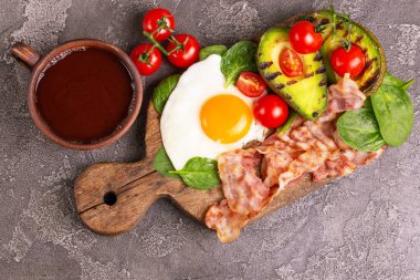 Izgara domuz pastırması ve avokado, ıspanak ve kiraz domates vintage ahşap kesme tahtası üzerinde sahanda yumurta. Gri beton zemin. Ketogenic diyet. Düşük carb yüksek yağ kahvaltı. Sağlıklı gıda kavramı