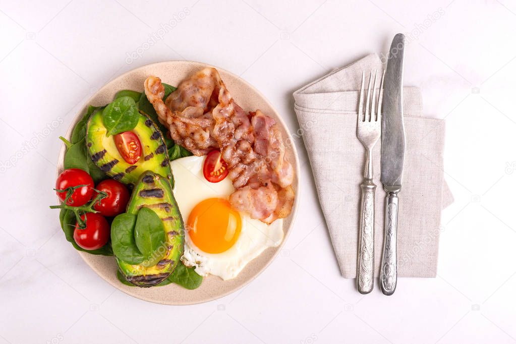 Grilled bacon and avocado, fried eggs with spinach and cherry tomatoes on light marble background. Ketogenic diet. Low carb high fat breakfast. Healthy food concept