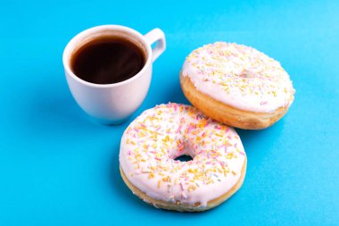 Serpin ve parlak mavi zemin üzerine kahve ile iki lezzetli vanilyalı donut. Sağlıksız, ama lezzetli tatlılar. Uzay kopyalayın. Yatay görünüm