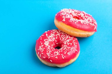 İki lezzetli pembe donut ile parlak mavi zemin üzerine serpin. Sağlıksız, ama lezzetli tatlılar. Uzay kopyalayın. Üstten görünüm