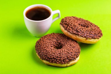 Serpin ve parlak yeşil zemin üzerine kahve ile iki lezzetli çikolatalı çörek. Sağlıksız, ama lezzetli tatlılar. Uzay kopyalayın. Üstten görünüm