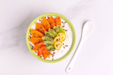 Kaşık ile Trabzon hurması, kivi, Kamkat ve keten tohumu ile vanilya acai kase. Açık renkli mermer. Sağlıklı gıda kavramı. Üstten görünüm