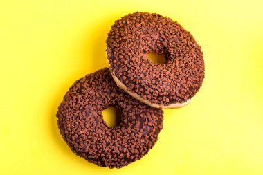 Two delicious chocolate donuts with sprinkle on bright yellow background. Unhealthy, but tasty sweets. Copy space. Top view
