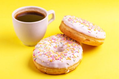 Serpin ve parlak sarı zemin üzerine kahve ile iki lezzetli vanilyalı donut. Sağlıksız, ama lezzetli tatlılar. Uzay kopyalayın. Yatay görünüm