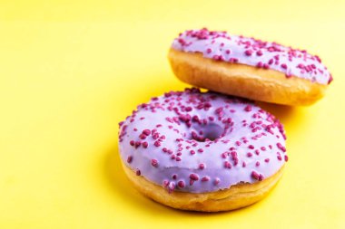 İki lezzetli leylak donut ile parlak sarı zemin üzerine serpin. Sağlıksız, ama lezzetli tatlılar. Uzay kopyalayın. Üstten görünüm