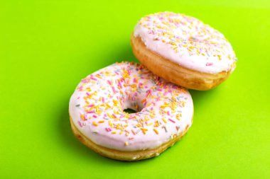 İki lezzetli vanilyalı donut ile parlak yeşil zemin üzerine serpin. Sağlıksız, ama lezzetli tatlılar. Uzay kopyalayın. Üstten görünüm