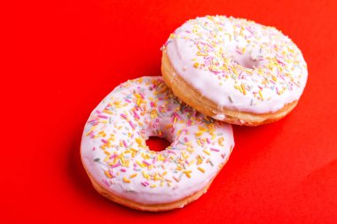 İki lezzetli vanilyalı donut ile parlak kırmızı zemin üzerine serpin. Sağlıksız, ama lezzetli tatlılar. Uzay kopyalayın. Üstten görünüm