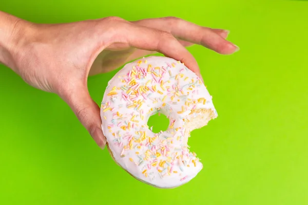 Bitten tasty vanilla donut with sprinkle in woman\'s hands. Bright colorful background. Unhealthy, but delicious sweets. Copy space. Top view