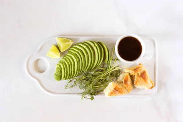 Ontbijt met avocado, broodje, erwten spruiten, limoen, pesto en koffie — Stockfoto