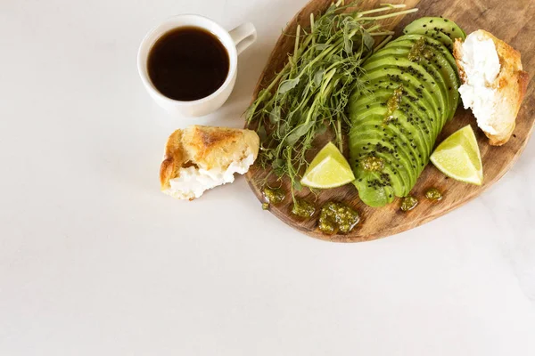 Ontbijt met avocado, broodje, erwten spruiten, limoen, pesto en koffie — Stockfoto