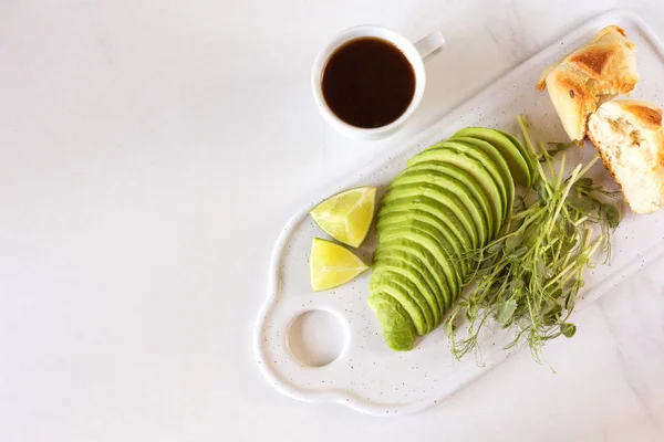 Ontbijt met avocado, broodje, erwten spruiten, limoen, pesto en koffie — Stockfoto