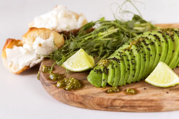 Ontbijt met avocado, broodje, erwten spruiten, limoen, pesto en koffie — Stockfoto