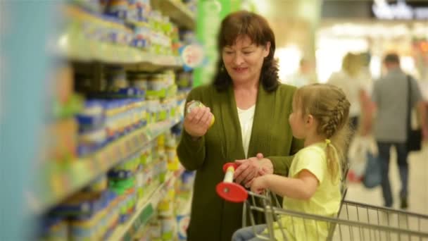 Babcia i wnuczka kupuje elementy w centrum handlowym. Wnuczka siedzi w wózek na zakupy. — Wideo stockowe