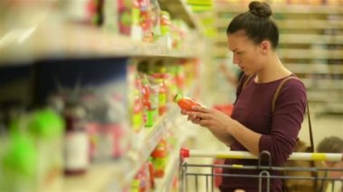 Genç kadın suyu süpermarket rafı seçer. O onun süpermarket arabası öğeleri bir sürü vardır.