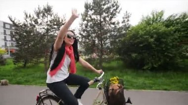 Bisiklet üzerinde mutlu genç kadın portresi. Onun bisiklet sepetinde çiçekler ve bir çanta var. O yolculuk sahiptir.