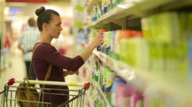 Güzel kadınlar sprey seçer. Yanında ürünleri ile bir süpermarket arabası.