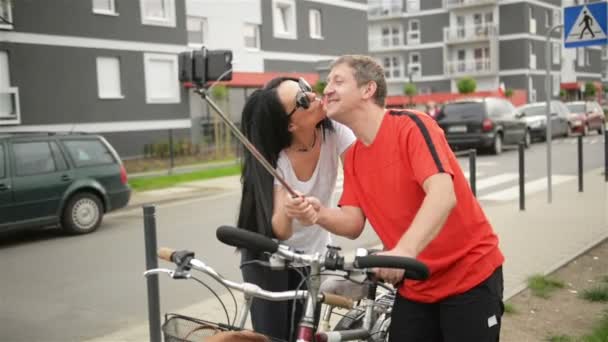 Feliz pareja adulta tomando selfie después de montar en bicicleta. Un Mab sostiene Smartphone en un palo. En este momento la niña abraza y coquetea con él . — Vídeo de stock