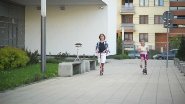 Flicka och pojke som rider Kick Scooter utomhus. Glad söt barn som leker på gatan lärande saldot på Kick Board på landsbygden. — Stockvideo