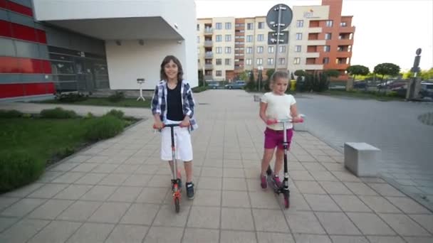 Niños felices están montando en patada Scooter al aire libre. Se divierten mucho jugando juntos . — Vídeo de stock