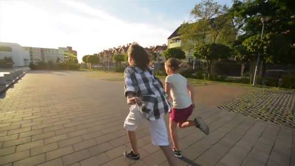 Gelukkige kinderen lopen samen bedrijf handen op de weg. De stralen van de zon stralen in hun gezichten. — Stockvideo