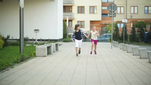 Мальчик и девочка бегут вместе по улице, держа за руки. They Have a lot of Fun . — стоковое видео