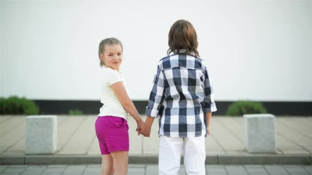 Ein paar kinder stehen zurück und halten sich an den händen. Lächelndes Mädchen winkt. — Stockvideo