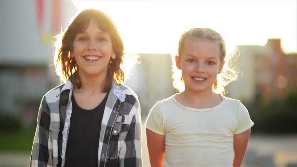 Retrato de dos niños felices sonriendo al aire libre. Los rayos del sol brillan en sus rostros . — Vídeos de Stock