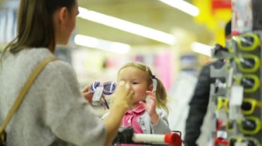 Portre portre çekici genç anne süpermarkette küçük kızıyla birlikte. Mutlu aile raf ayakta hipermarket içinde güneş gözlüğü seçiminde.
