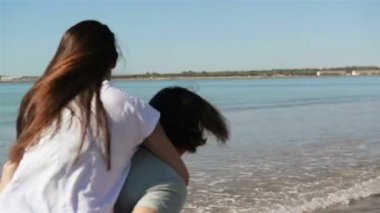 Genç komik çift sahilde Piggybacking güneş gözlüğü. Arkadaşlar eğlenmeye birlikte. Deniz arka plan üzerinde olduğunu.