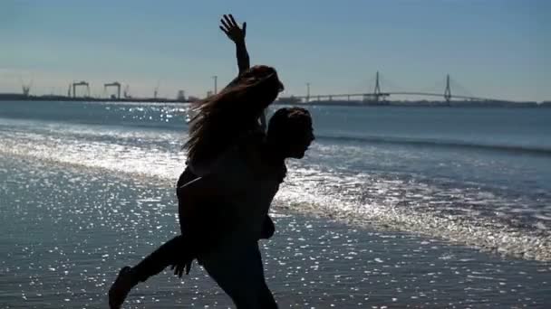 Jonge grappige paar in zonnebril meeliften op het strand. Vrienden samen plezier. Zee is op achtergrond. — Stockvideo