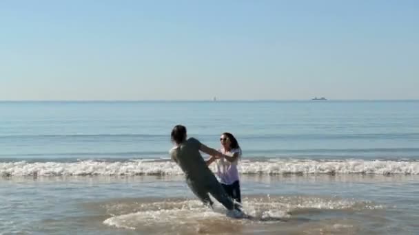 Pareja de amigos sosteniendo las manos y divirtiéndose. Tienen apariencia caucásica. Mar con olas está en el fondo — Vídeos de Stock