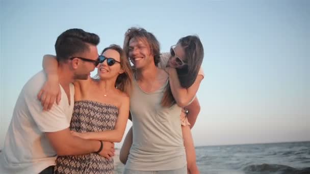 Aktive vier Personen, die im Sommerurlaub bei windigem Wetter am Strand spazieren gehen und den Sonnenuntergang genießen. — Stockvideo